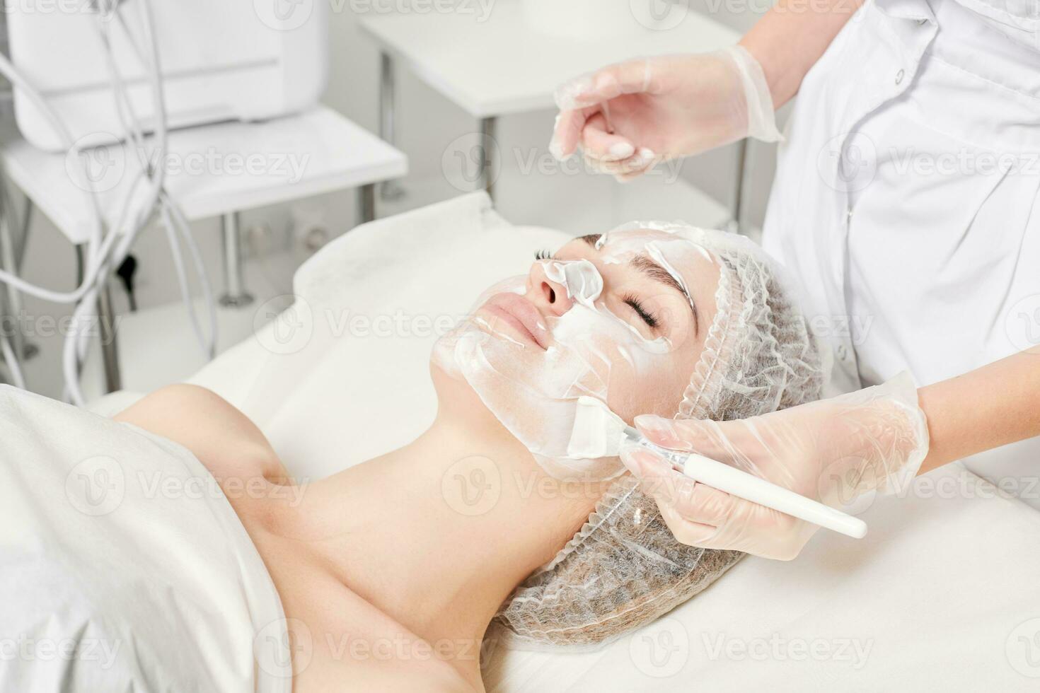 Beautician applies cream mask on woman face for rejuvenation face skin, procedure in beauty salon photo