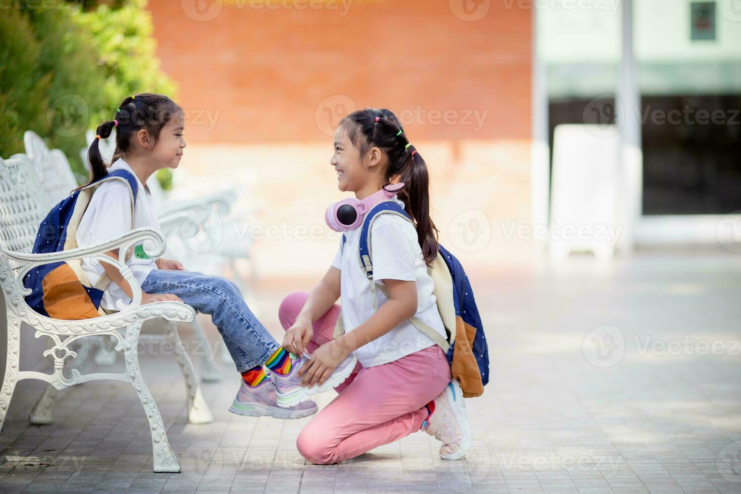 espalda a escuela. linda pequeño niña amabilidad corbatas cordones de los zapatos para un amigo. foto