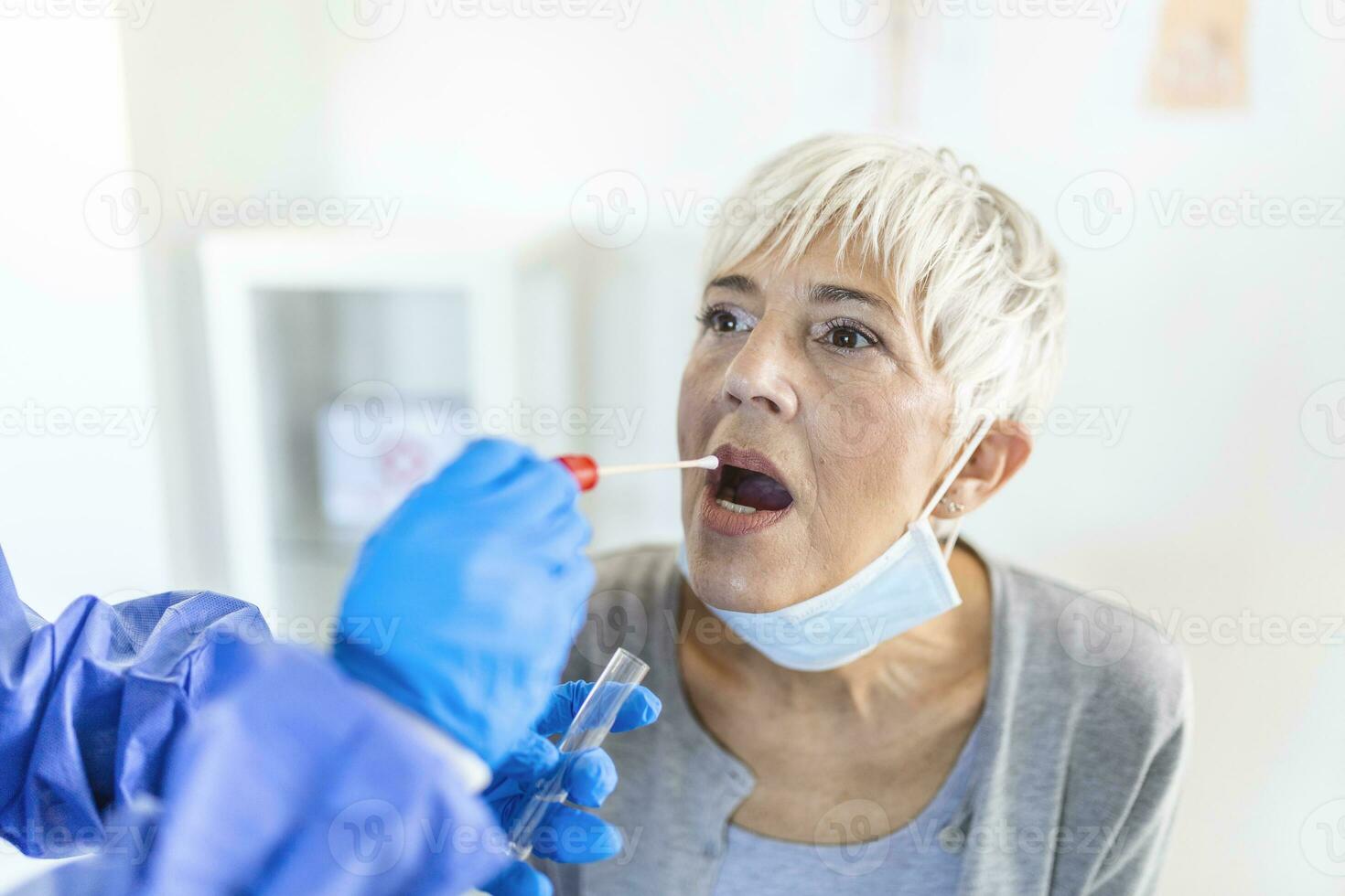 Physician wearing personal protective equipment performing a Coronavirus COVID-19 PCR test, patient nasal NP and oral OP swab sample specimen collection process, viral rt-PCR DNA diagnostic procedure photo