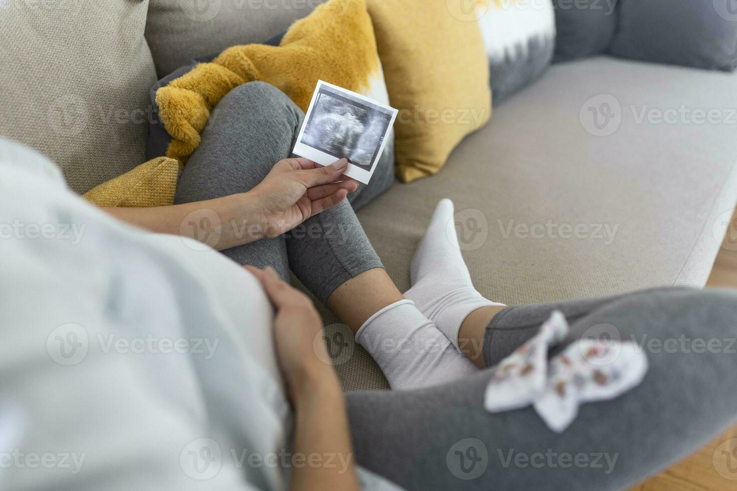 Pregnant woman holding ultrasound image. Concept of pregnancy, health care, gynecology, medicine. Young mother waiting of the baby. Close-up, copy space, indoors. photo