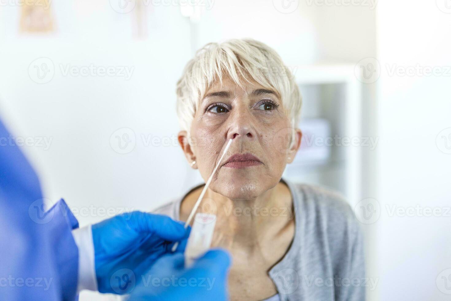 Healthcare worker with protective equipment performs coronavirus swab on mature woman.Nose swab for Covid-19. photo
