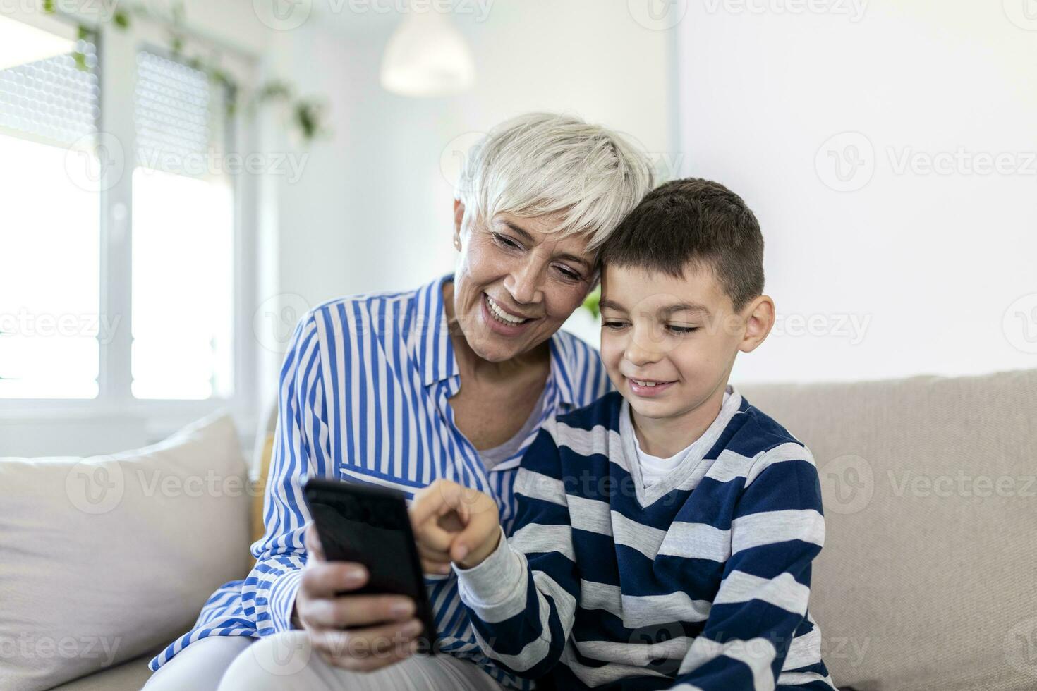 Happy grandmother and grandson using tablet together, sitting on cozy sofa at home, browsing tablet device apps, grandma with grandchild playing game, looking at screen, having fun photo