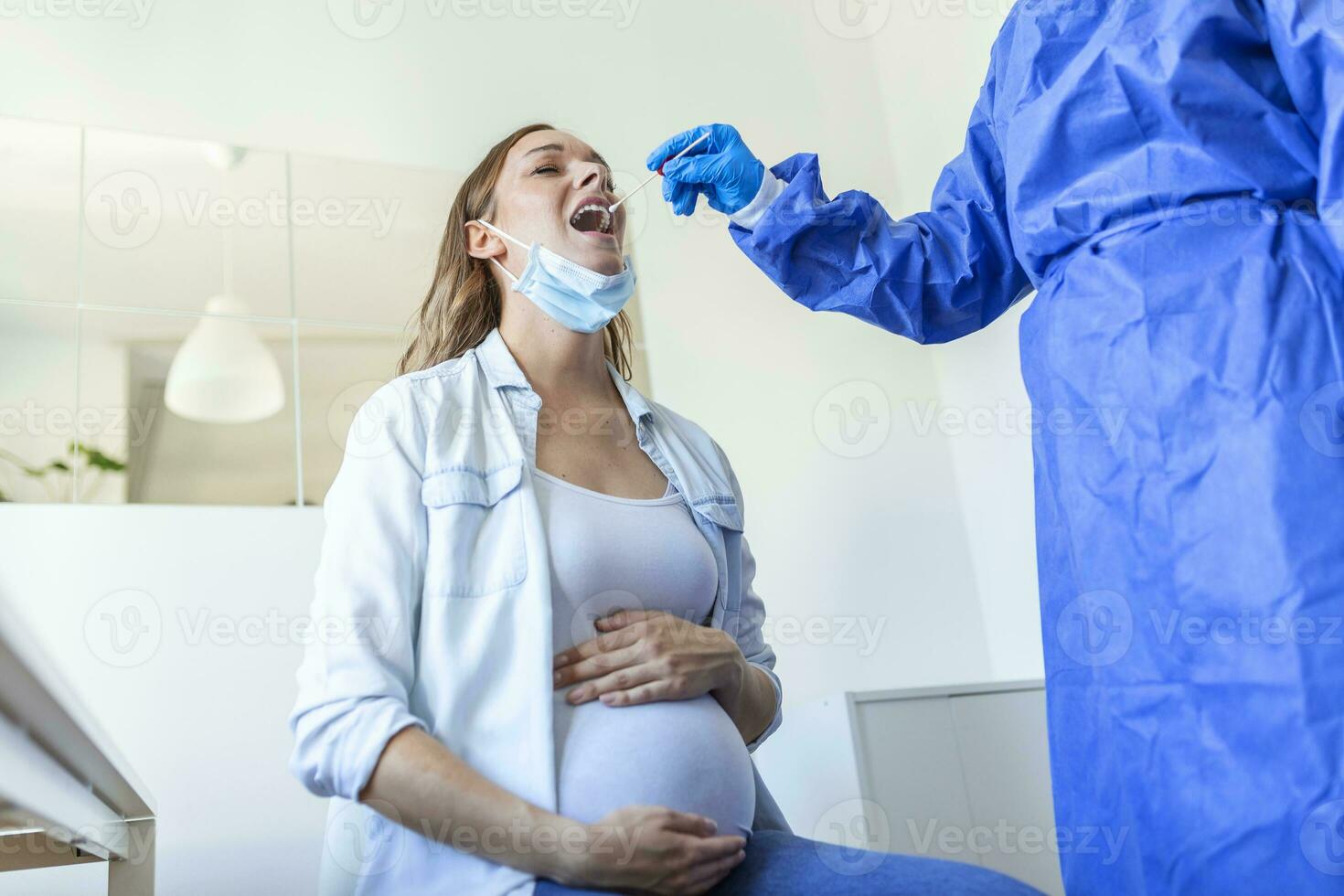 Physician wearing personal protective equipment performing a Coronavirus COVID-19 PCR test, pregnant woman nasal NP and oral OP swab sample specimen collection process, viral rt-PCR DNA procedure photo