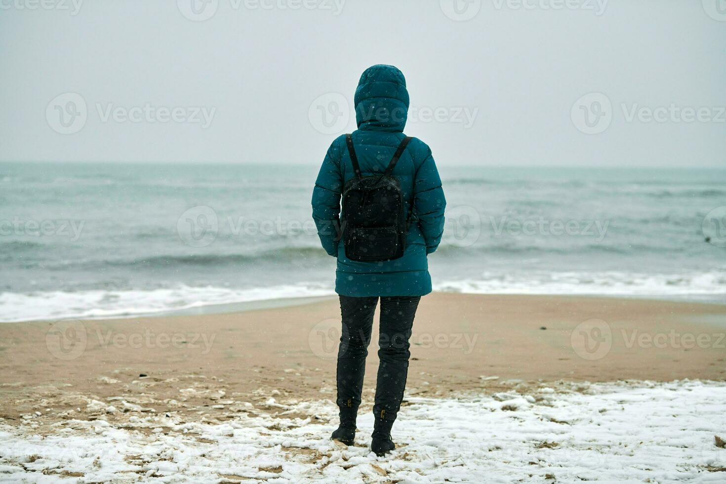 Girl in down jacket standing on seashore in winter photo