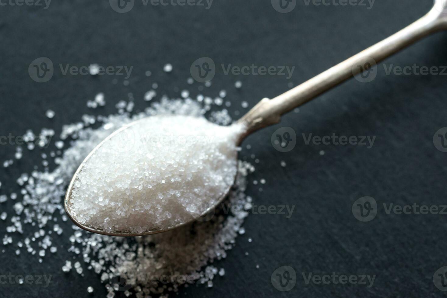 Spoon with white sugar on the dark background photo