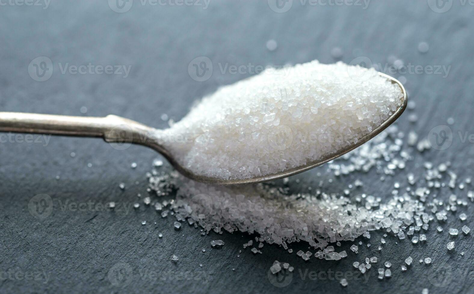 Spoon with white sugar on the dark background photo