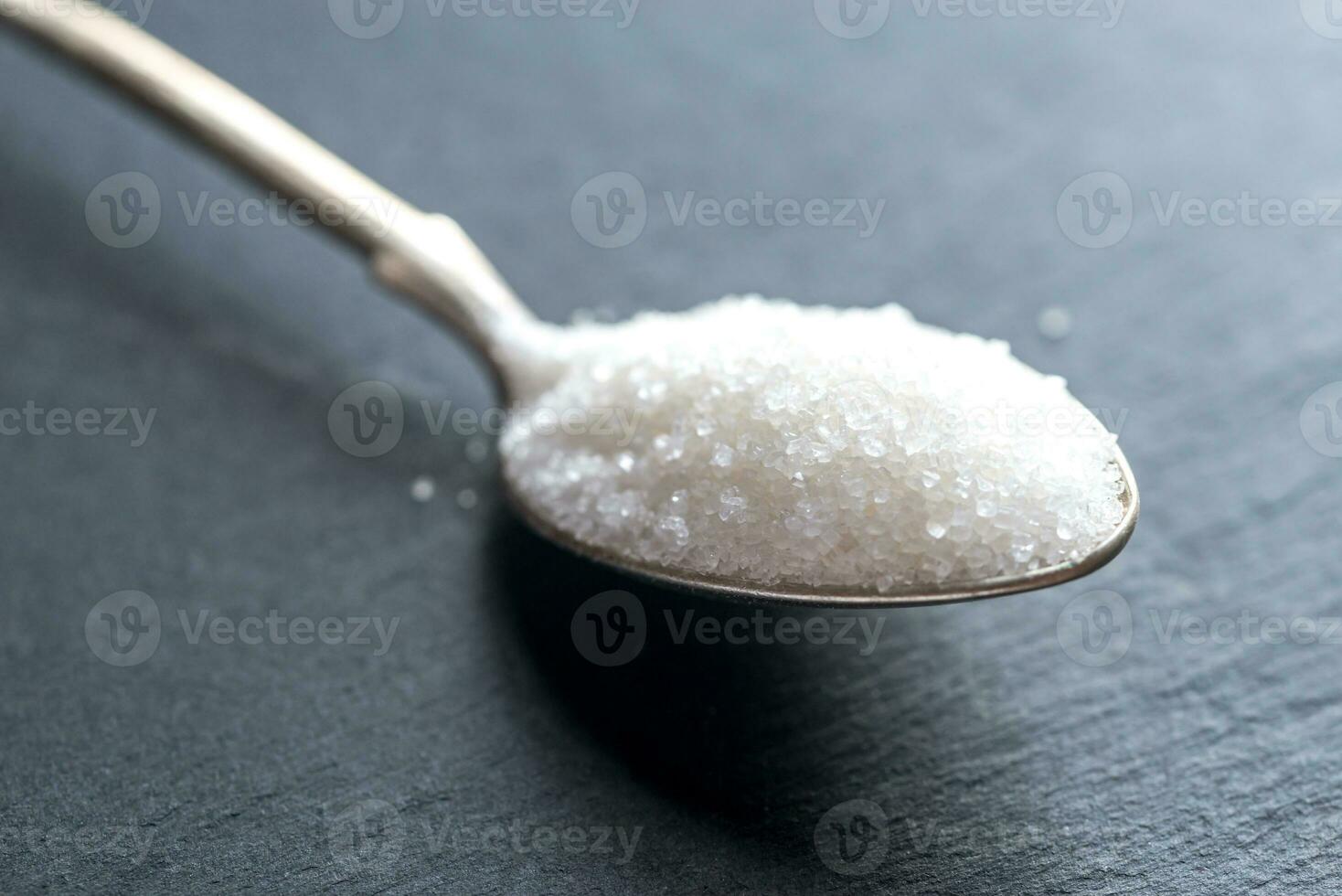 Spoon with white sugar on the dark background photo