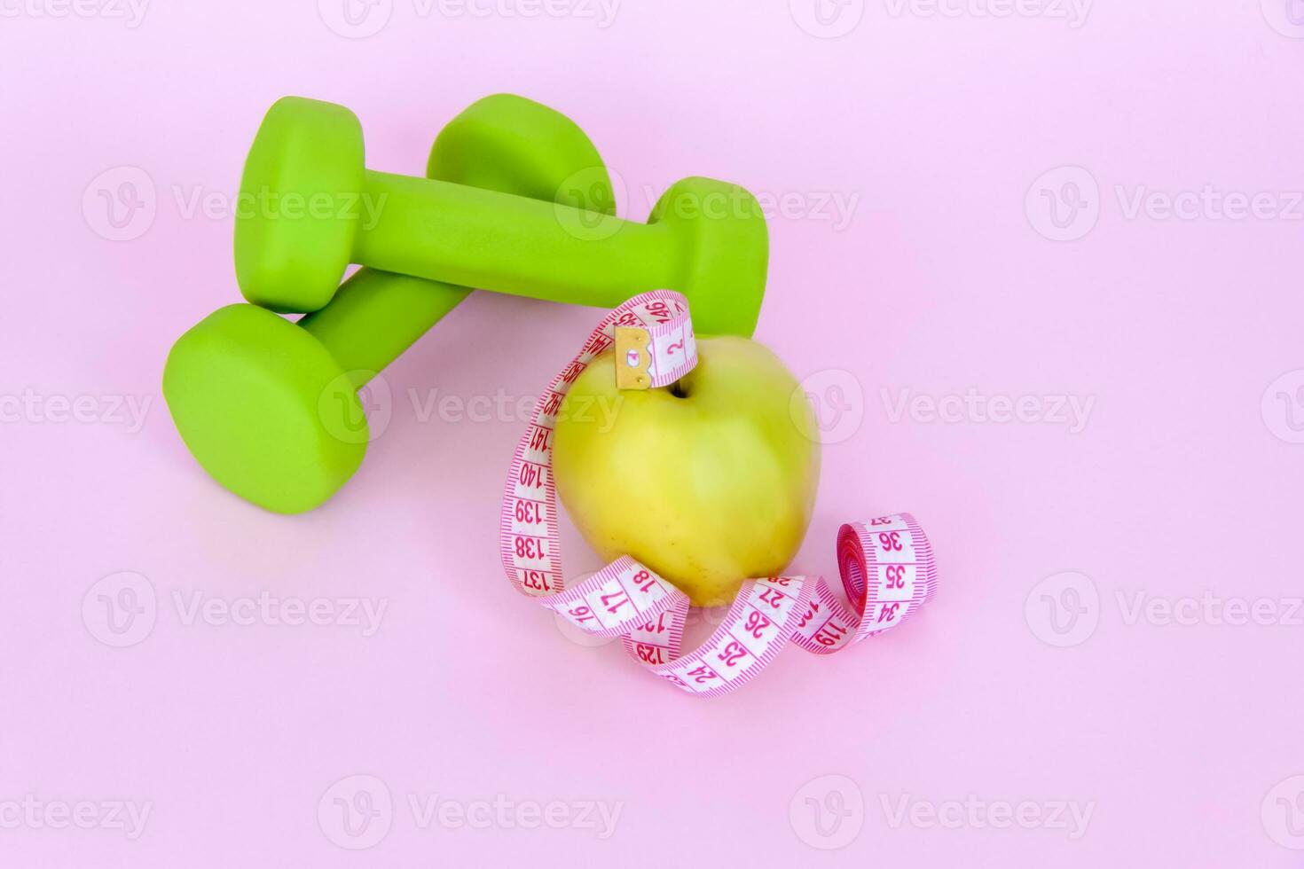 A green apple, and a centimeter measuring tape on a pink background. Sports, sports nutrition, healthy eating, diet. Space for the text. photo