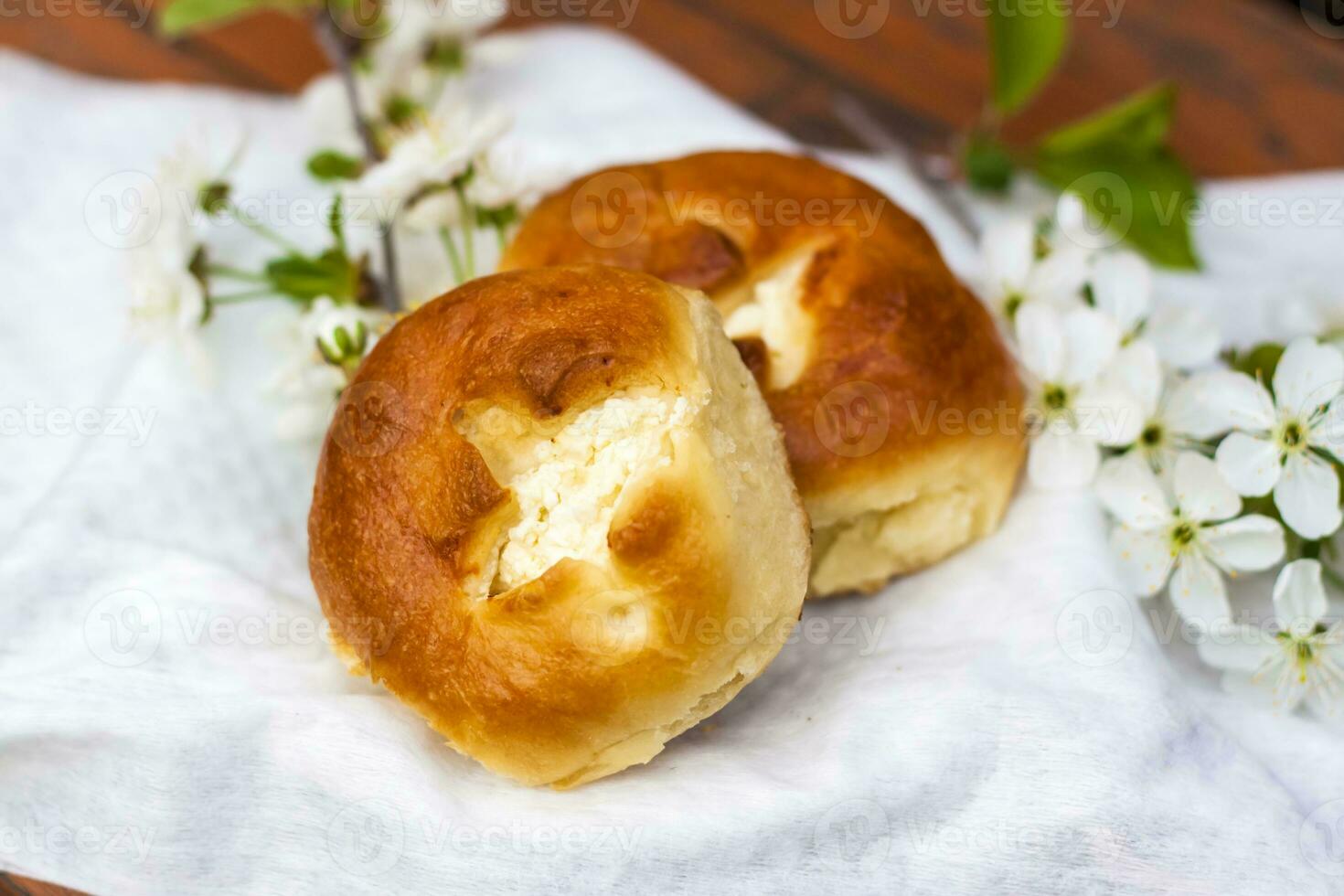 Baked open rolls on a dark, worn rustic wooden table. The composition is decorated with a twig with white flowers. Cherry tree flowers. Selective focus. photo