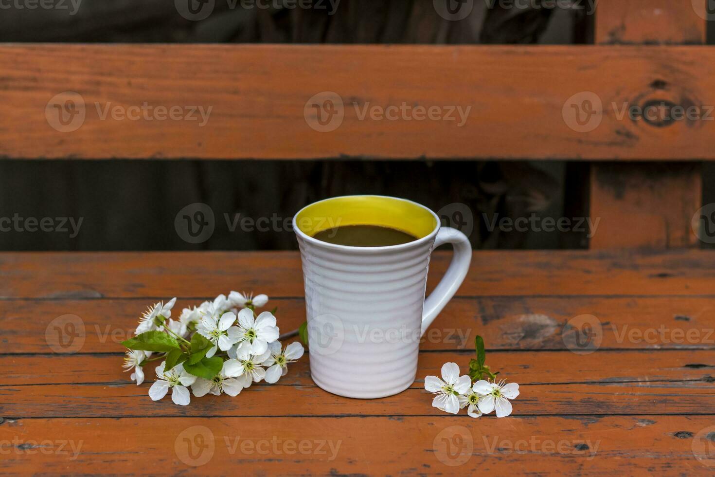 a cup of coffee on a dark, worn rustic wooden table. The composition is decorated with a twig with white flowers. Cherry tree flowers. Selective focus. photo