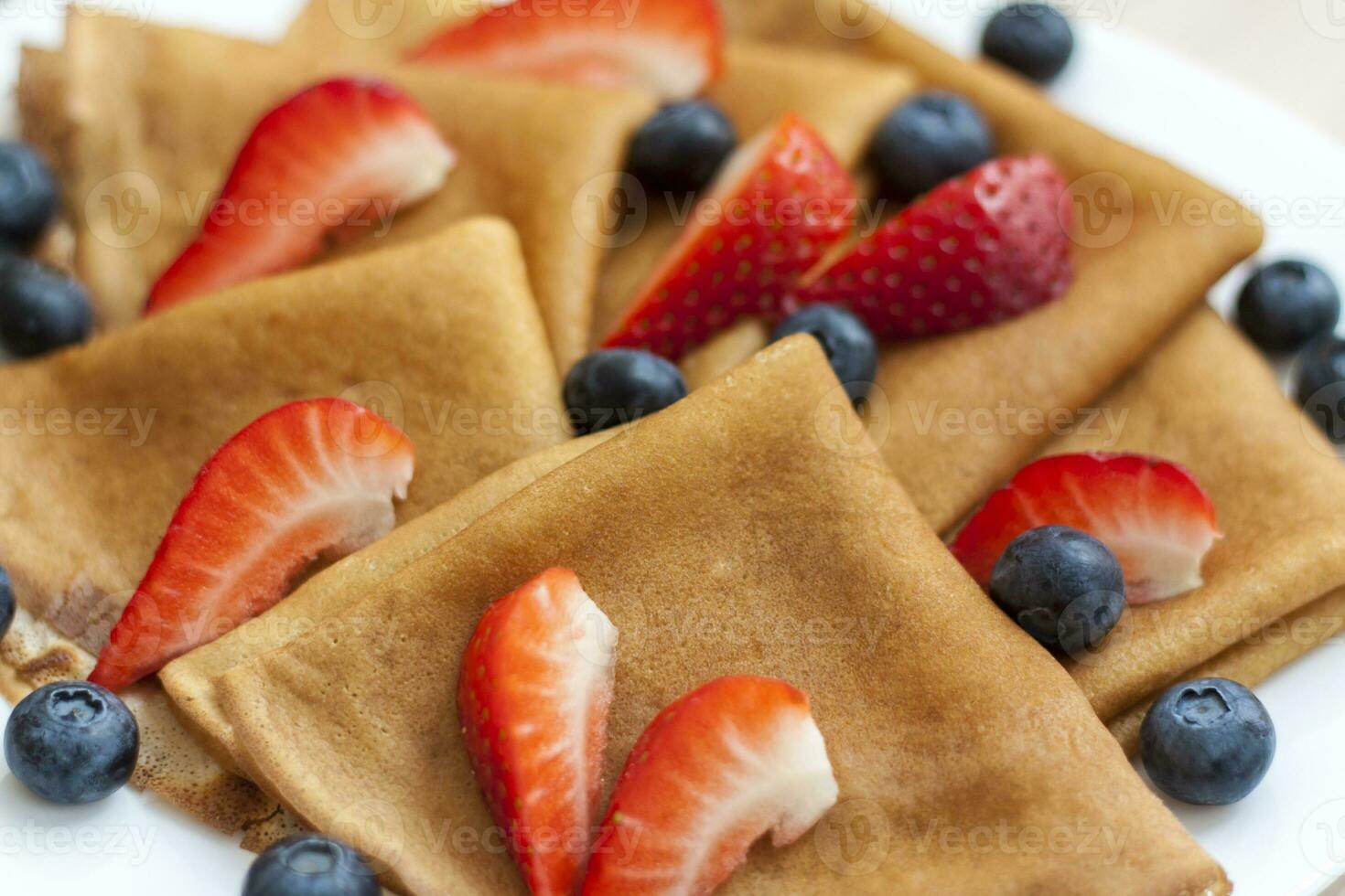 Pancakes with blueberries and strawberries on the table. Traditional food for Maslenitsa photo