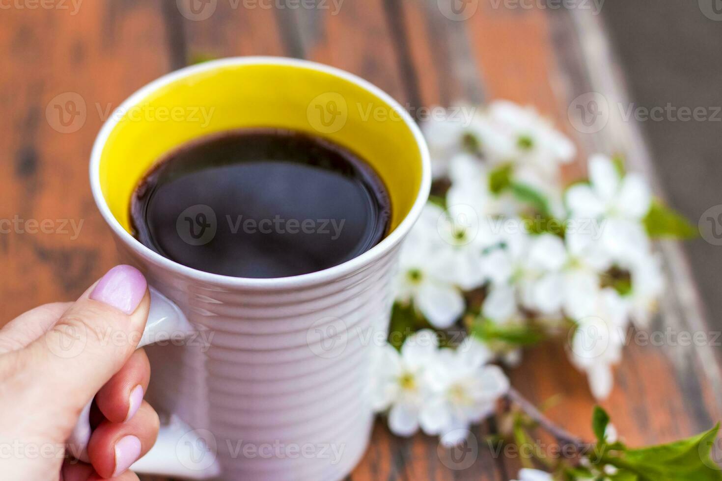 a cup of coffee on a dark, worn rustic wooden table. The composition is decorated with a twig with white flowers. Cherry tree flowers. Selective focus. photo