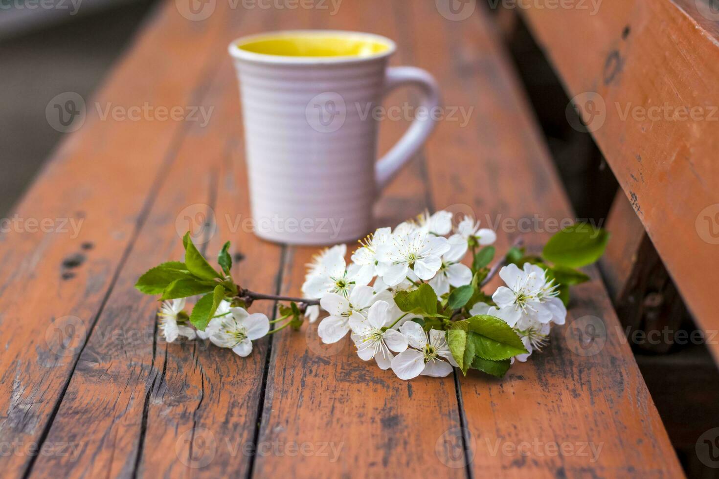 a cup of coffee on a dark, worn rustic wooden table. The composition is decorated with a twig with white flowers. Cherry tree flowers. Selective focus. photo