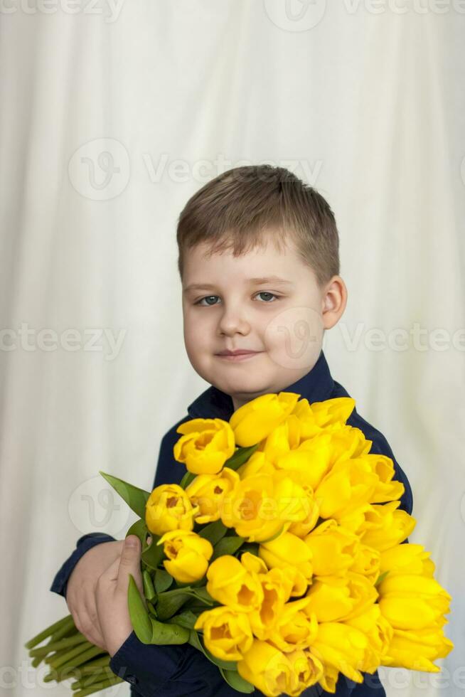 Portrait of a young, beautiful boy. Holds a huge armful of fresh yellow tulips. The concept of spring and holiday, March 8, International Women's Day photo