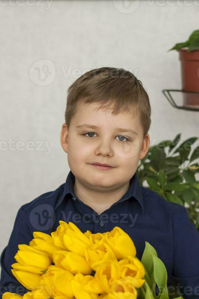 Portrait of a young, beautiful boy. Holds a huge armful of fresh yellow tulips. The concept of spring and holiday, March 8, International Women's Day, photo
