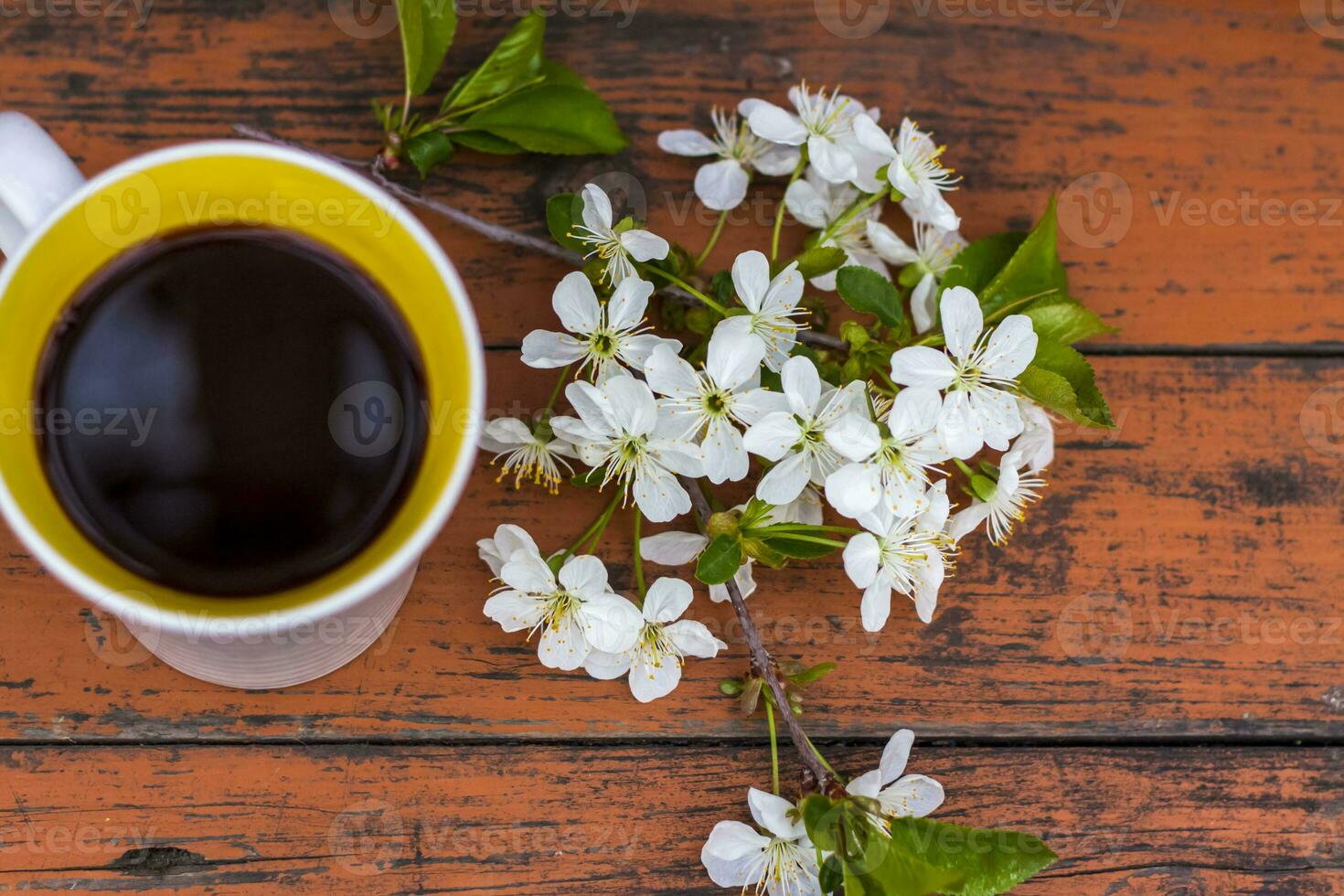 a cup of coffee on a dark, worn rustic wooden table. The composition is decorated with a twig with white flowers. Cherry tree flowers. Selective focus. photo