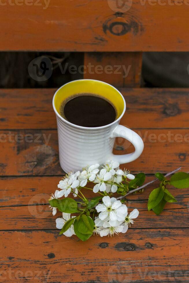 a cup of coffee on a dark, worn rustic wooden table. The composition is decorated with a twig with white flowers. Cherry tree flowers. Selective focus. photo