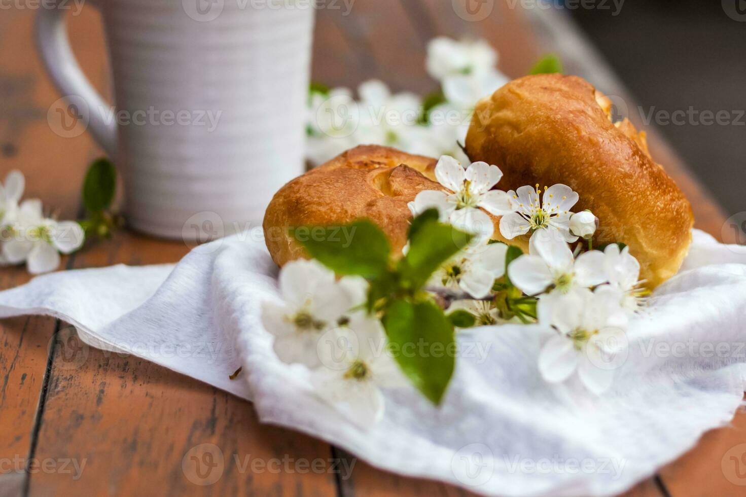 Baked open rolls and a cup of coffee on a dark, worn rustic wooden table. The composition is decorated with a twig with white flowers. Cherry tree flowers. Selective focus. photo