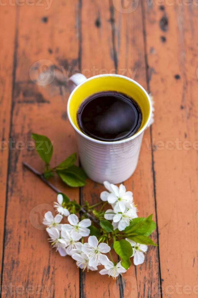 a cup of coffee on a dark, worn rustic wooden table. The composition is decorated with a twig with white flowers. Cherry tree flowers. Selective focus. photo