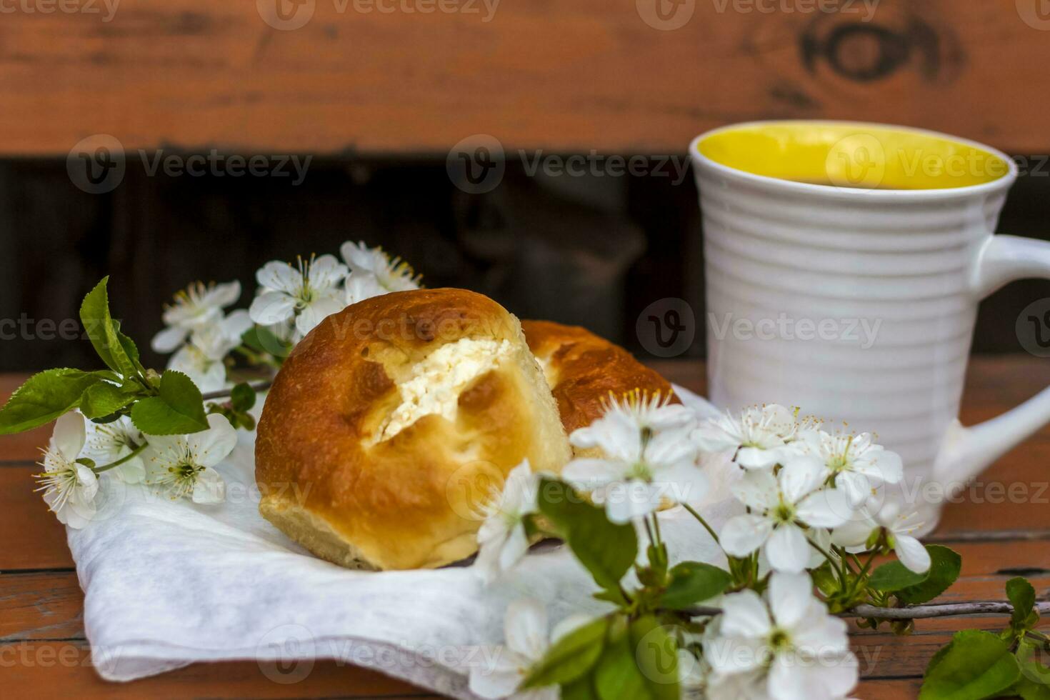 Baked open rolls and a cup of coffee on a dark, worn rustic wooden table. The composition is decorated with a twig with white flowers. Cherry tree flowers. Selective focus. photo