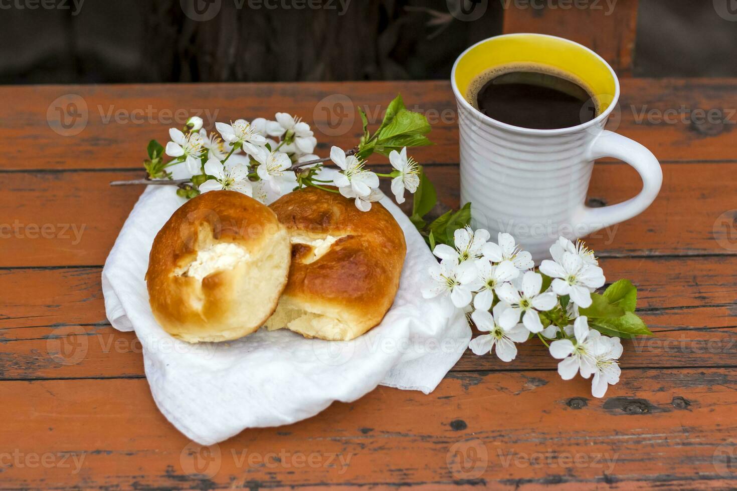 Baked open rolls and a cup of coffee on a dark, worn rustic wooden table. The composition is decorated with a twig with white flowers. Cherry tree flowers. Selective focus. photo