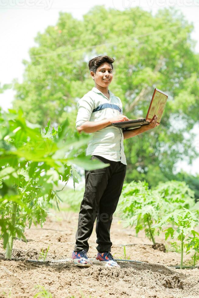 indio chico estudiando en granja, participación ordenador portátil en mano , pobre indio niños foto