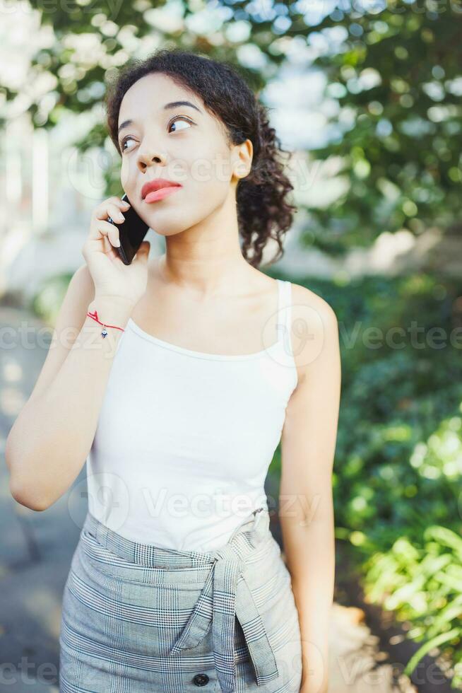 joven africano mujer Hablando en móvil teléfono. blanco t camisa Bosquejo foto