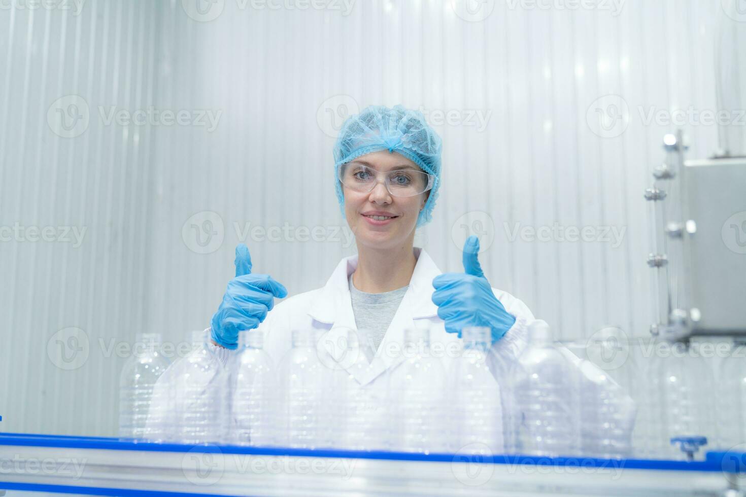 Portrait thumbs up of smiling Caucasian technologist expert standing by an automated machine for PET water production in a bottling factory. photo