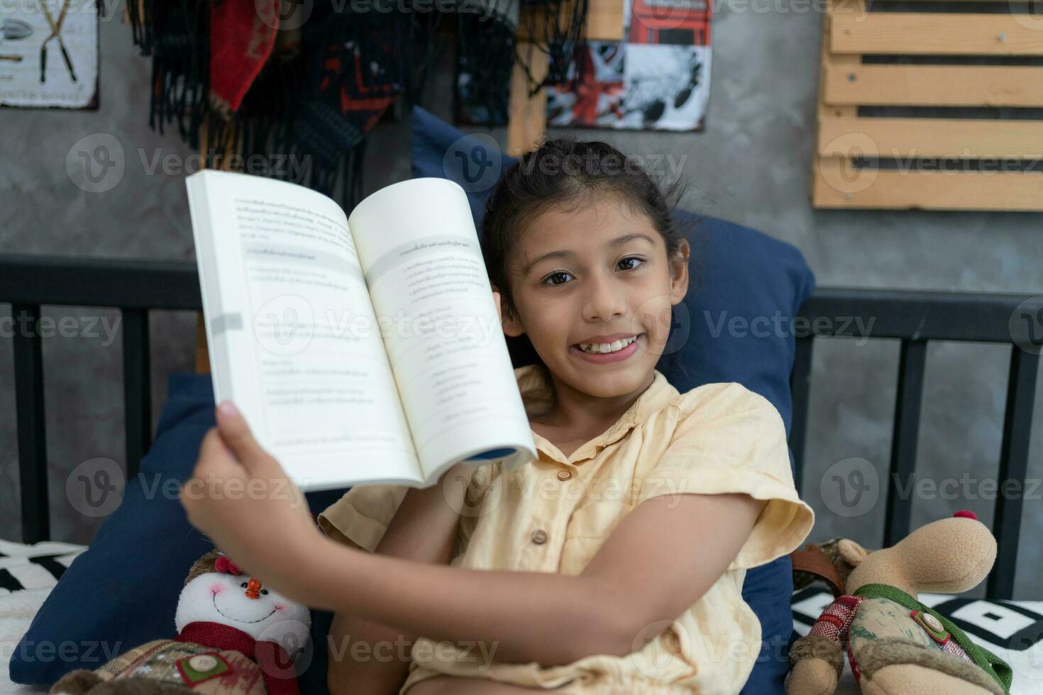 Portrait of cute little Reading A Book Doing Homework At Home. Happy Kid Girl Learning Sitting On Couch In Living Room Indoors. Educational Leisure And Hobby Concept photo