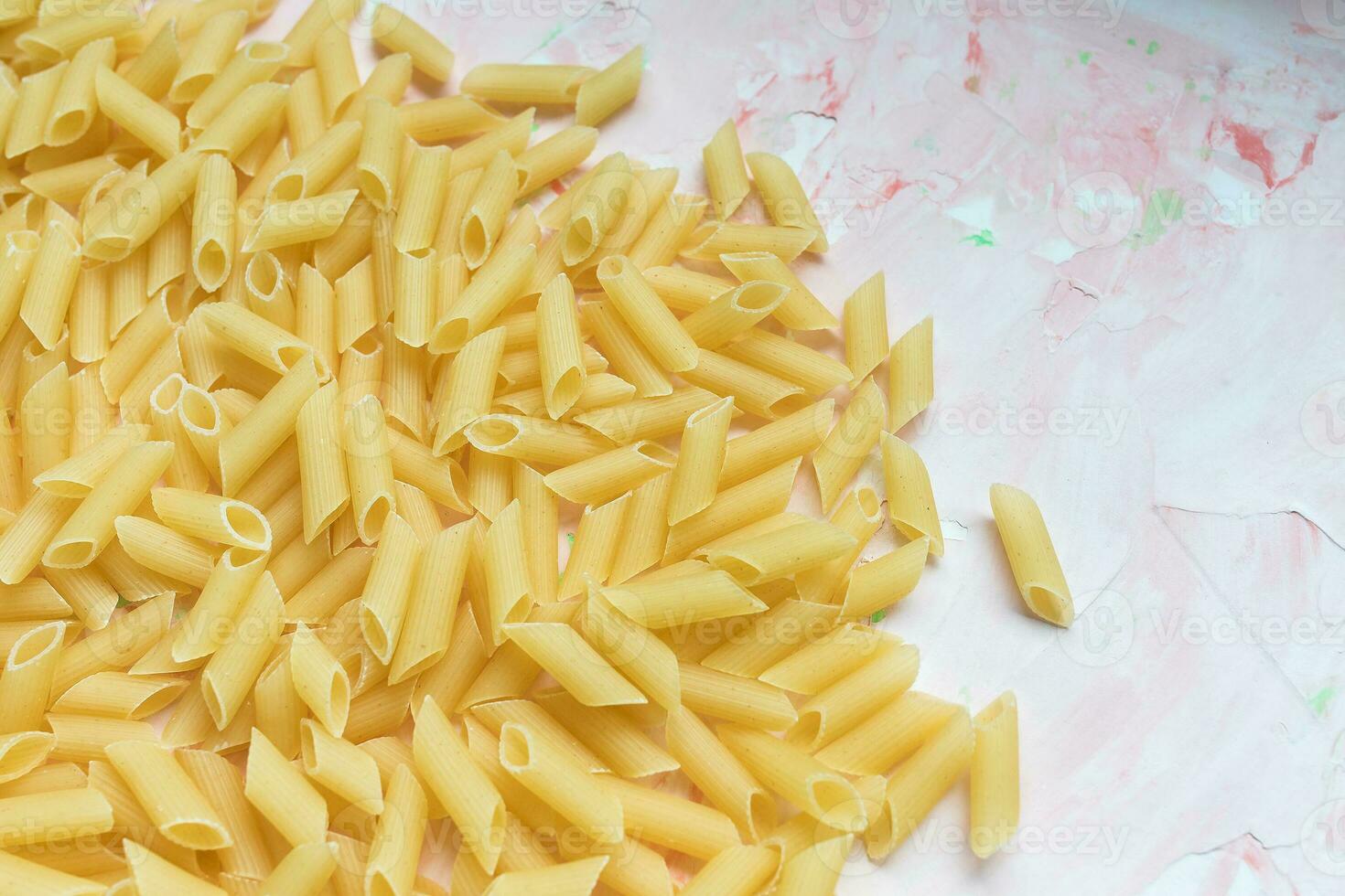 Raw Italian penne pasta on pink background photo