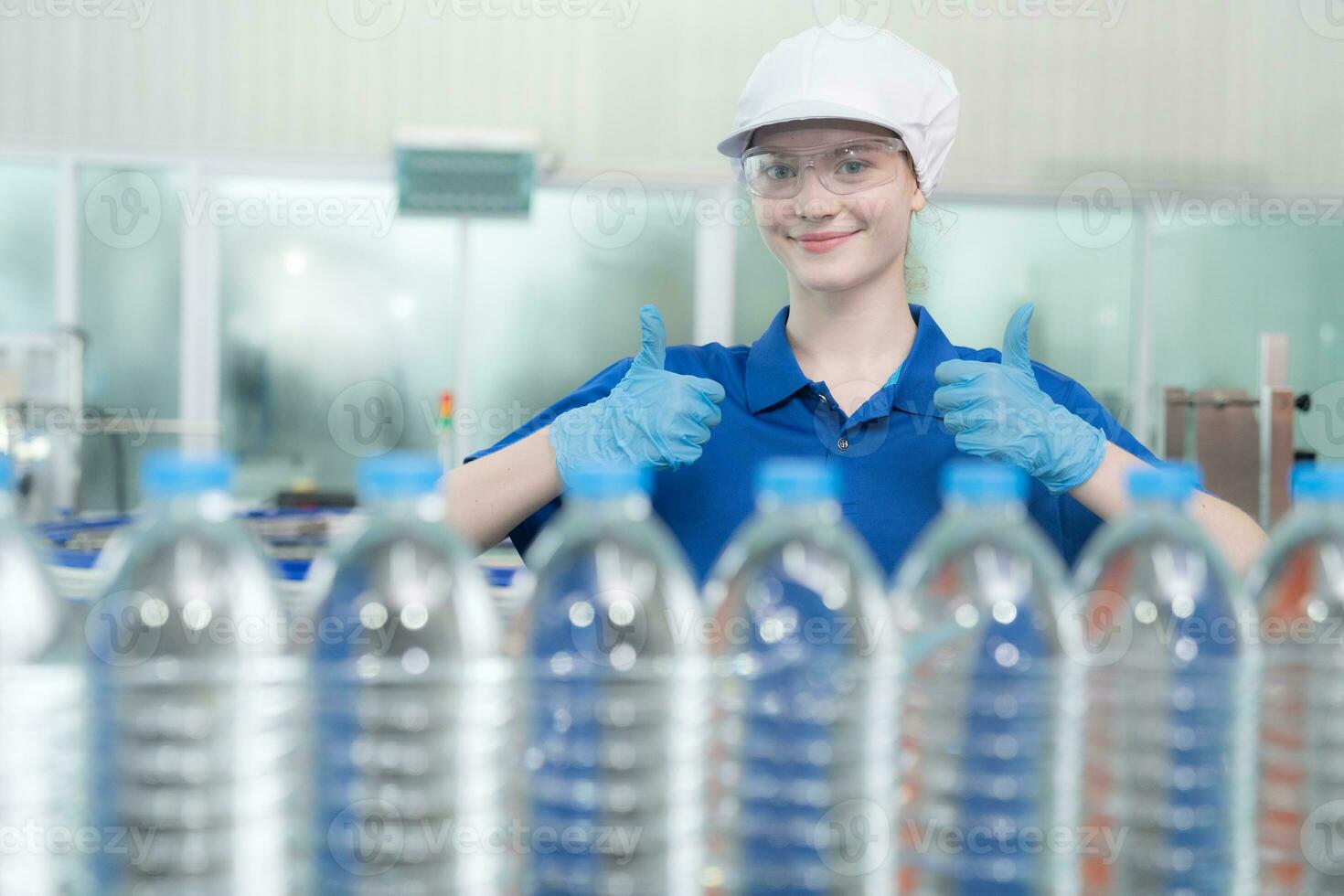 Portrait thumbs up of smiling Caucasian technologist expert standing by an automated machine for PET water production in a bottling factory. photo