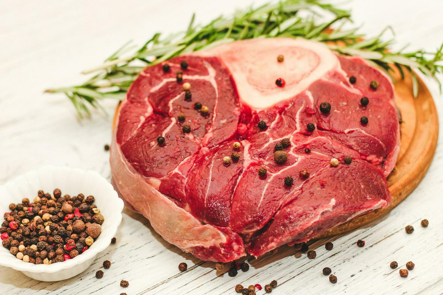 Fresh piece of meat large beef steak on the bone ossobuco with a sprig of rosemary on a black background photo