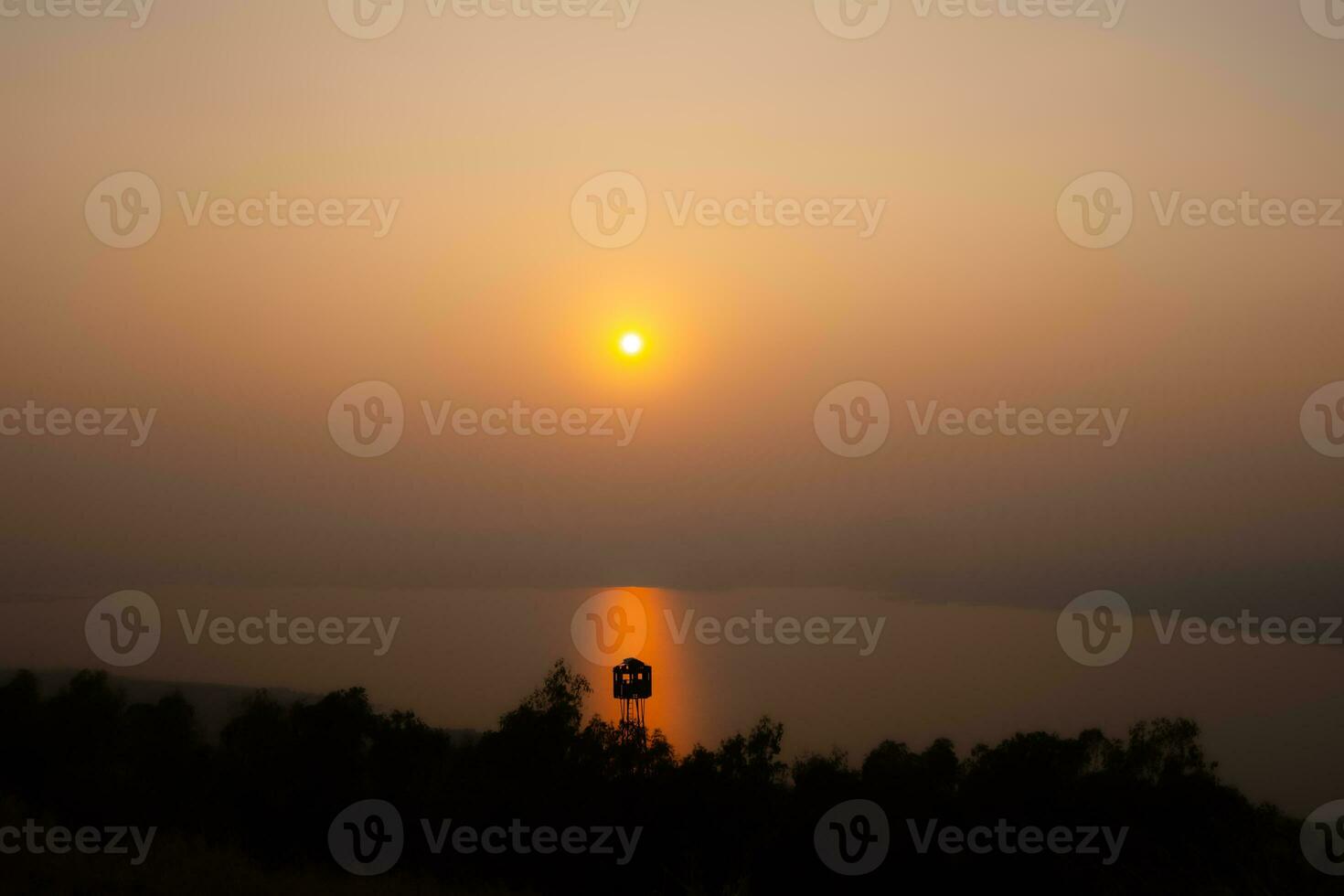 The river in Nakhon Ratchasima province where the sun is setting through the thick fog behind the mountains, giving rise to the orange color of the sun in the evening. photo