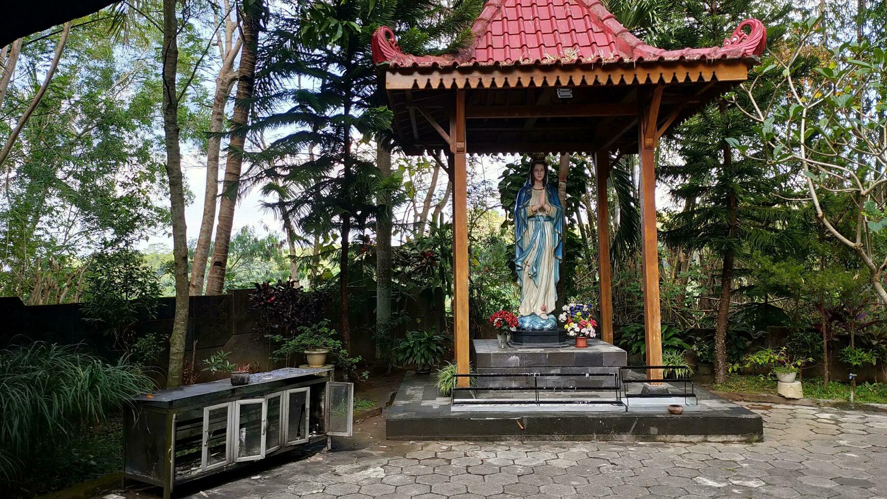 Statue of the Virgin Mary under a canopy with trees in the background, in the Jatiningsih Maria Cave, Jogjakarta, where Catholics pray, give thanks and submit requests to God photo