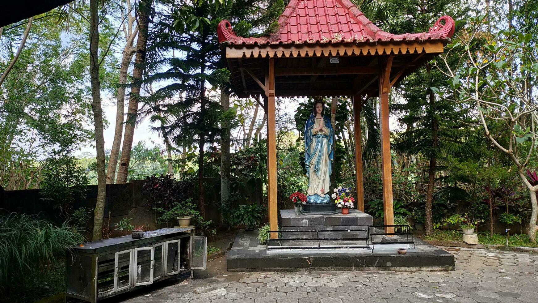 estatua de el Virgen María debajo un pabellón con arboles en el fondo, en el jatiningsih maria cueva, jogjakarta, dónde católicos orar, dar Gracias y enviar peticiones a Dios foto