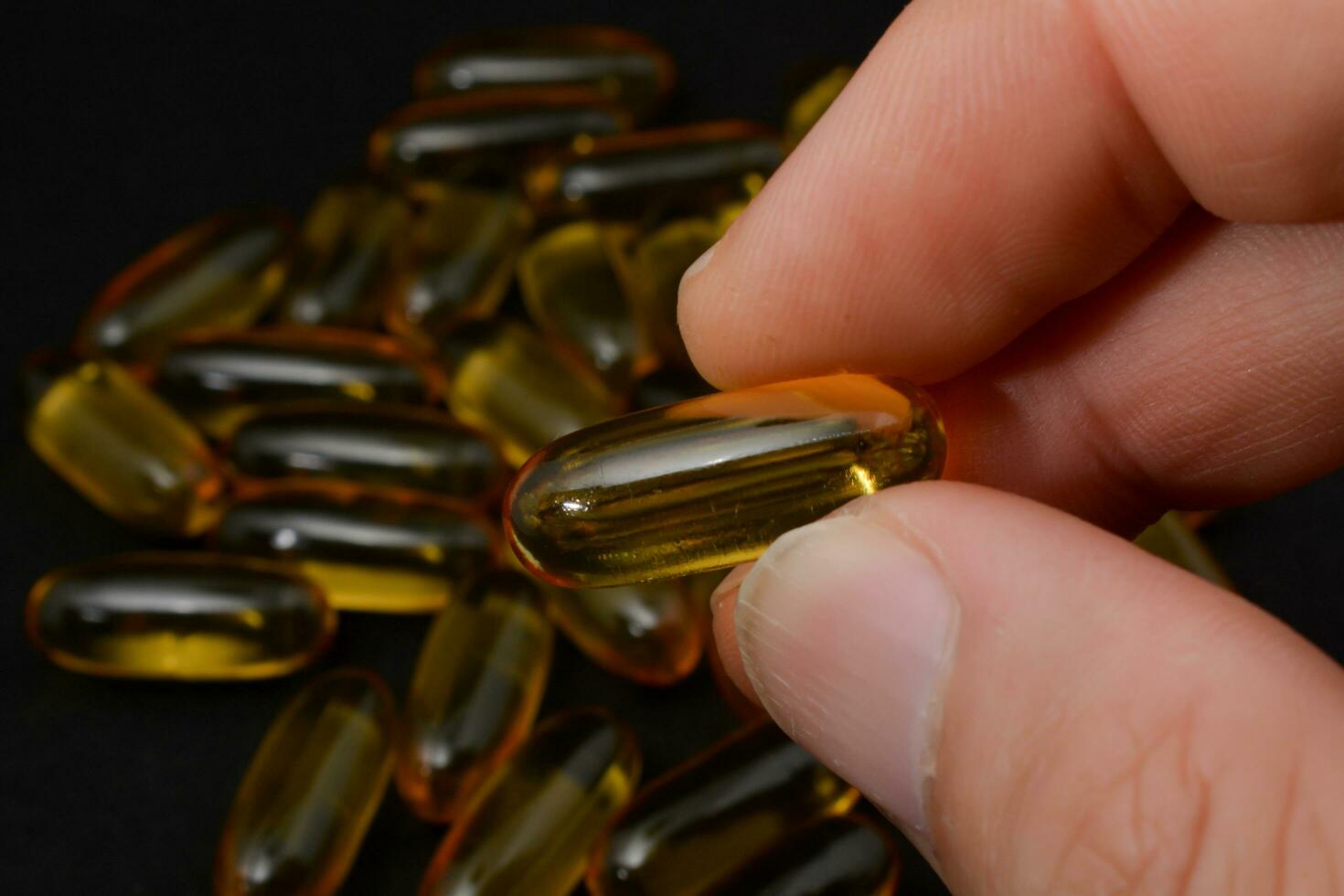 Fish oil in clear yellow capsules. For taking supplements, on male hands, isolate, black background photo