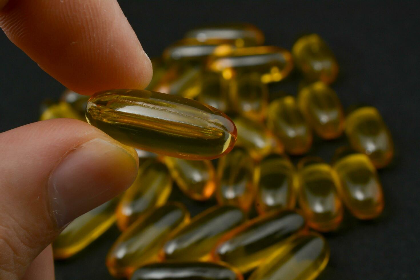 Fish oil in clear yellow capsules. For taking supplements, on male hands, isolate, black background photo