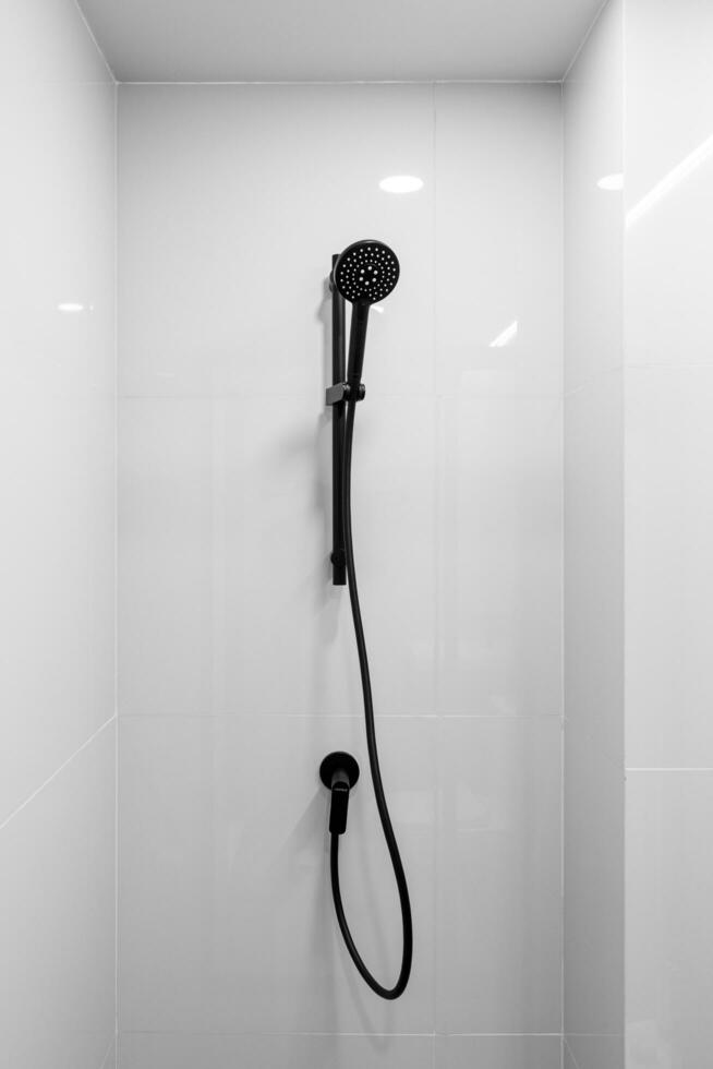 Black shower head on holder against tiled wall on background. Concept of white bathroom in modern Condo photo