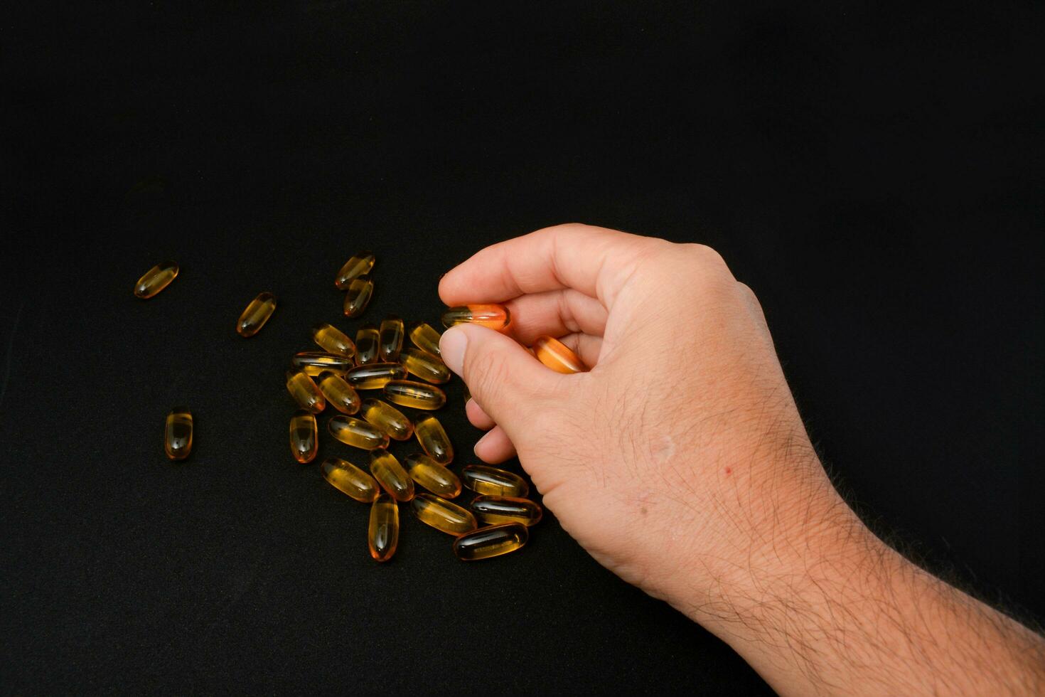 Fish oil in clear yellow capsules. For taking supplements, on male hands, isolate, black background photo