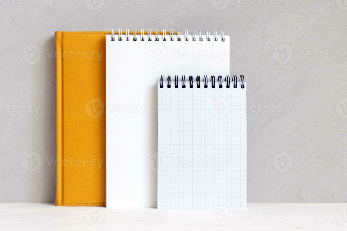 Notebooks are on shelf near gray wall. Empty sheet, mockup, copy space. photo
