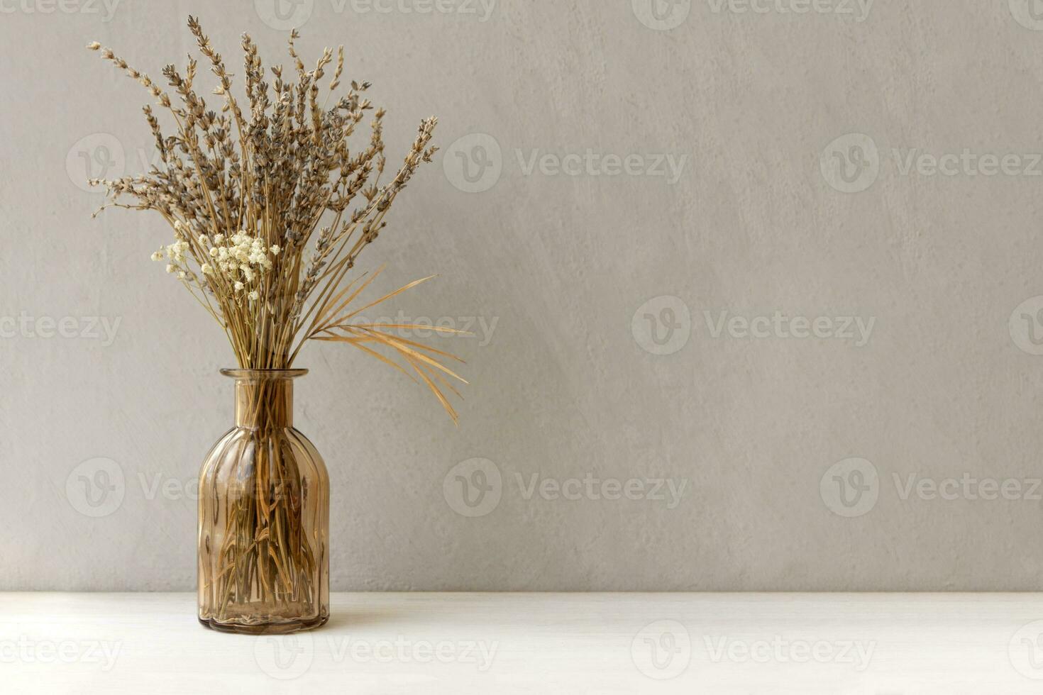 Minimalistic composition of dried flowers in glass brown vase on gray vintage textured wall background and on wooden shelf. Front view, mock up, copy space. photo