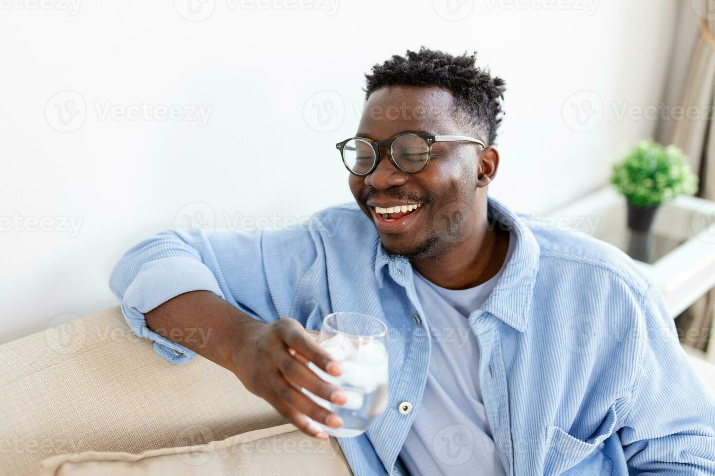 joven africano hombre en ropa casual Bebiendo agua desde vaso foto