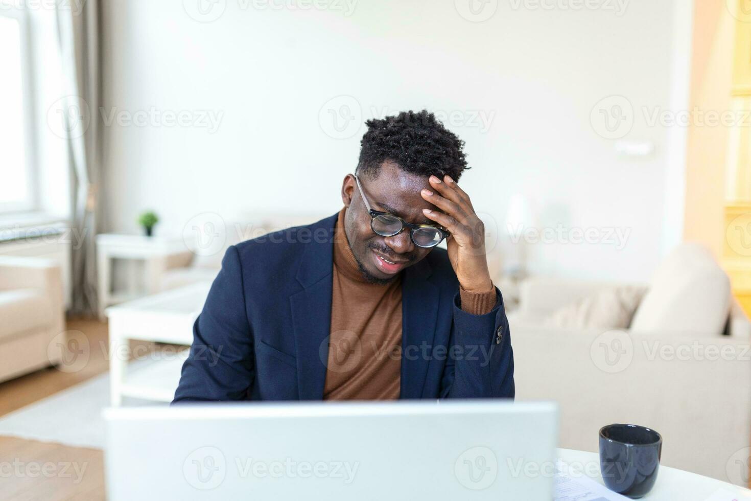 Stressed-out young businessman sitting with his head in his hands while working at a desk in an office. Portrait of frustrated young man with laptop working indoors, home office concept. photo