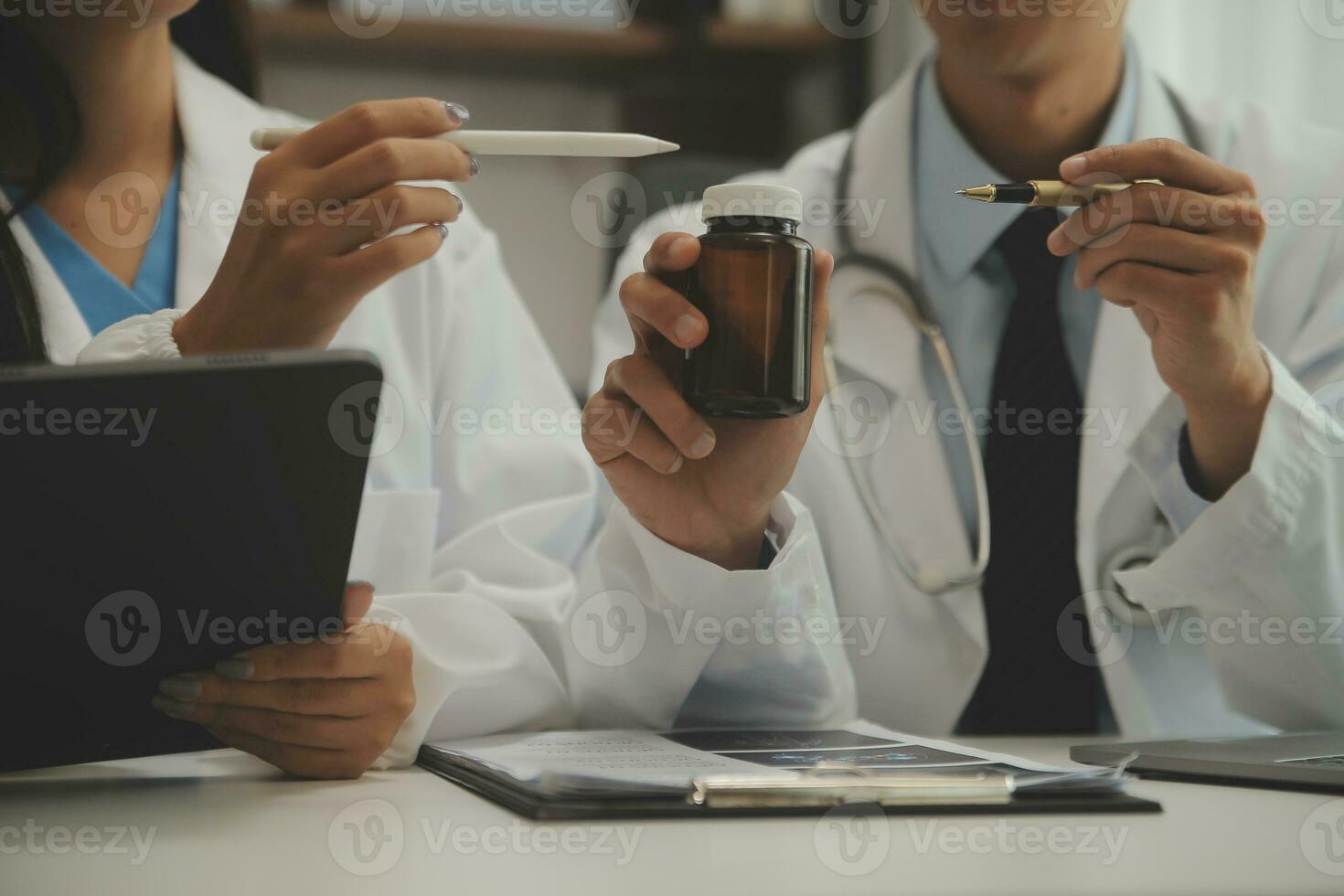 Confident doctor man holding a pill bottle and writing while talking with senior patient and reviewing his medication at office room. photo
