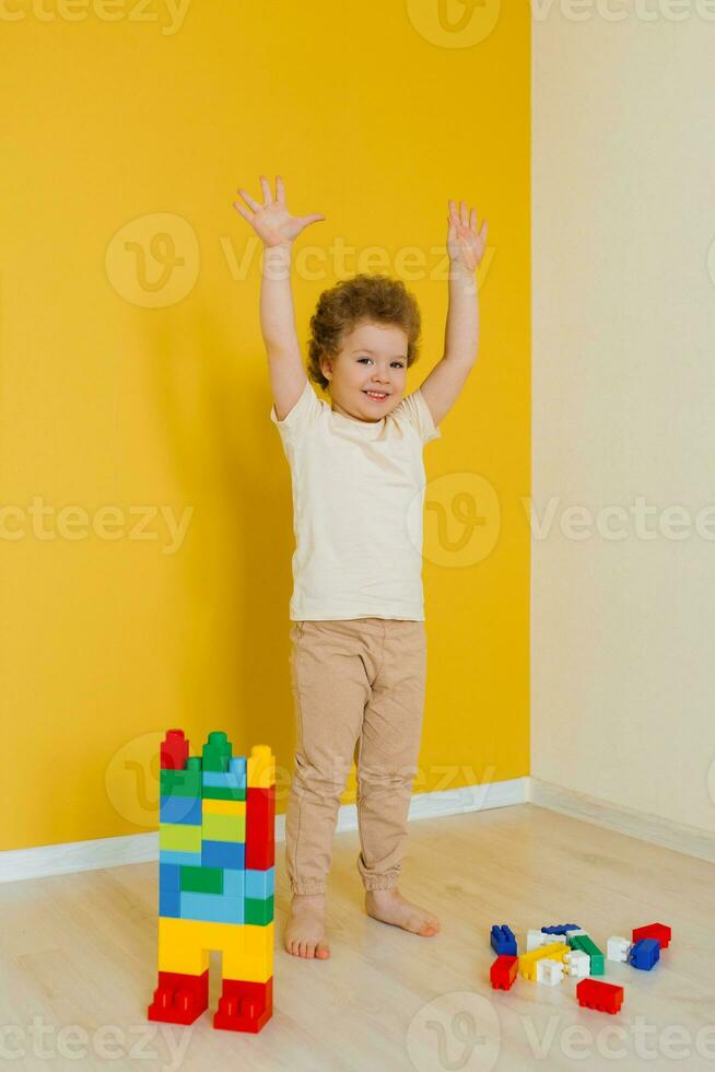 Child raised his hands up while standing on the floor and playing with the wooden multi-colored blocks of the car. Exercise for the brain and coordination of movements. Pre-school employment photo