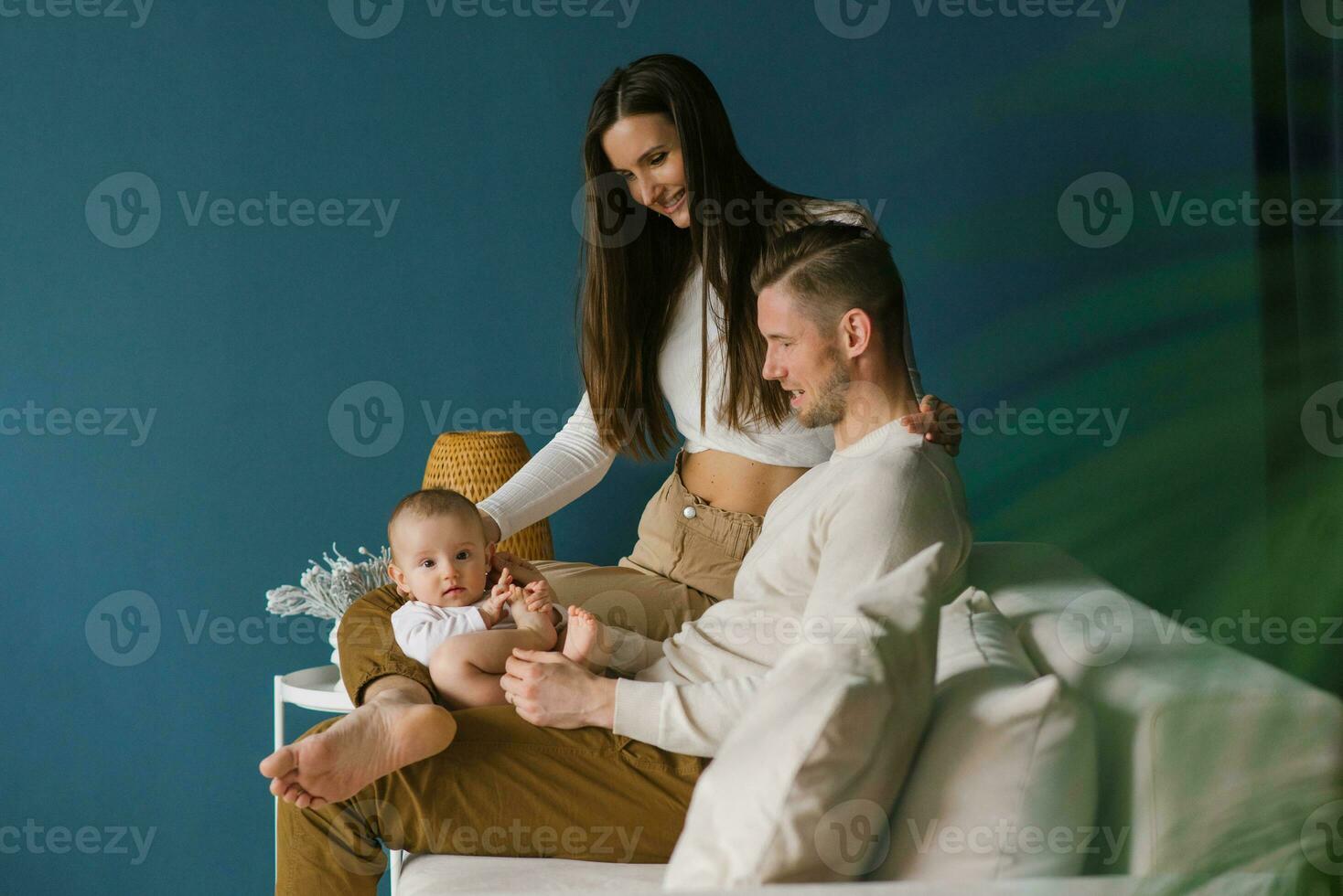 Happy positive family of the Caucasian race, a young father and mother, a little son are resting at home, sitting on a sofa against a blue wall. photo