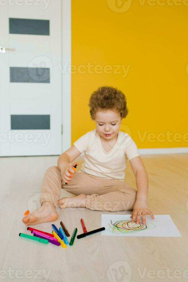 linda pequeño chico es sentado a hogar en el piso y dibujo un dibujo con de colores Lápices niño desarrollo y creatividad para preescolares y primario colegio niños en jardín de infancia o a hogar foto