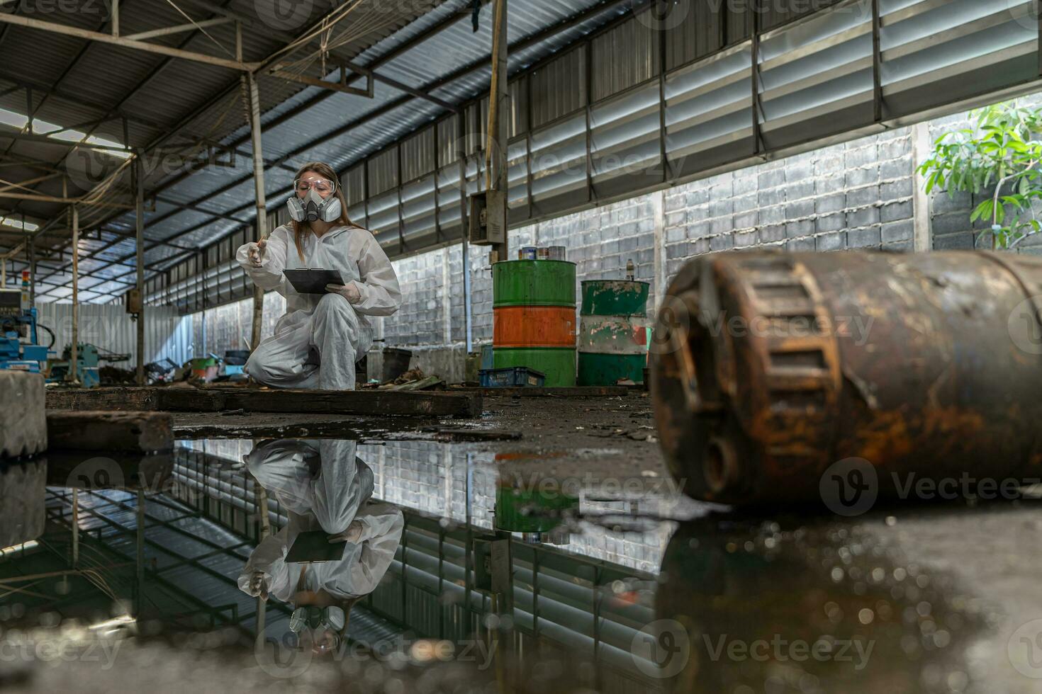 emergency pollution factory concept. Female chemist wearing PPE and gas mask inspecting oil on factory floor photo