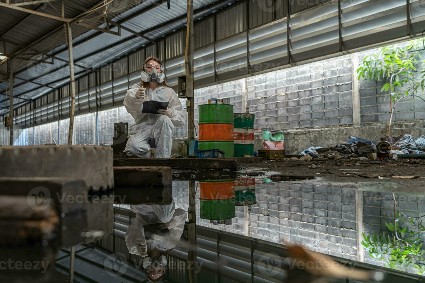 emergency pollution factory concept. Female chemist wearing PPE and gas mask inspecting oil on factory floor photo