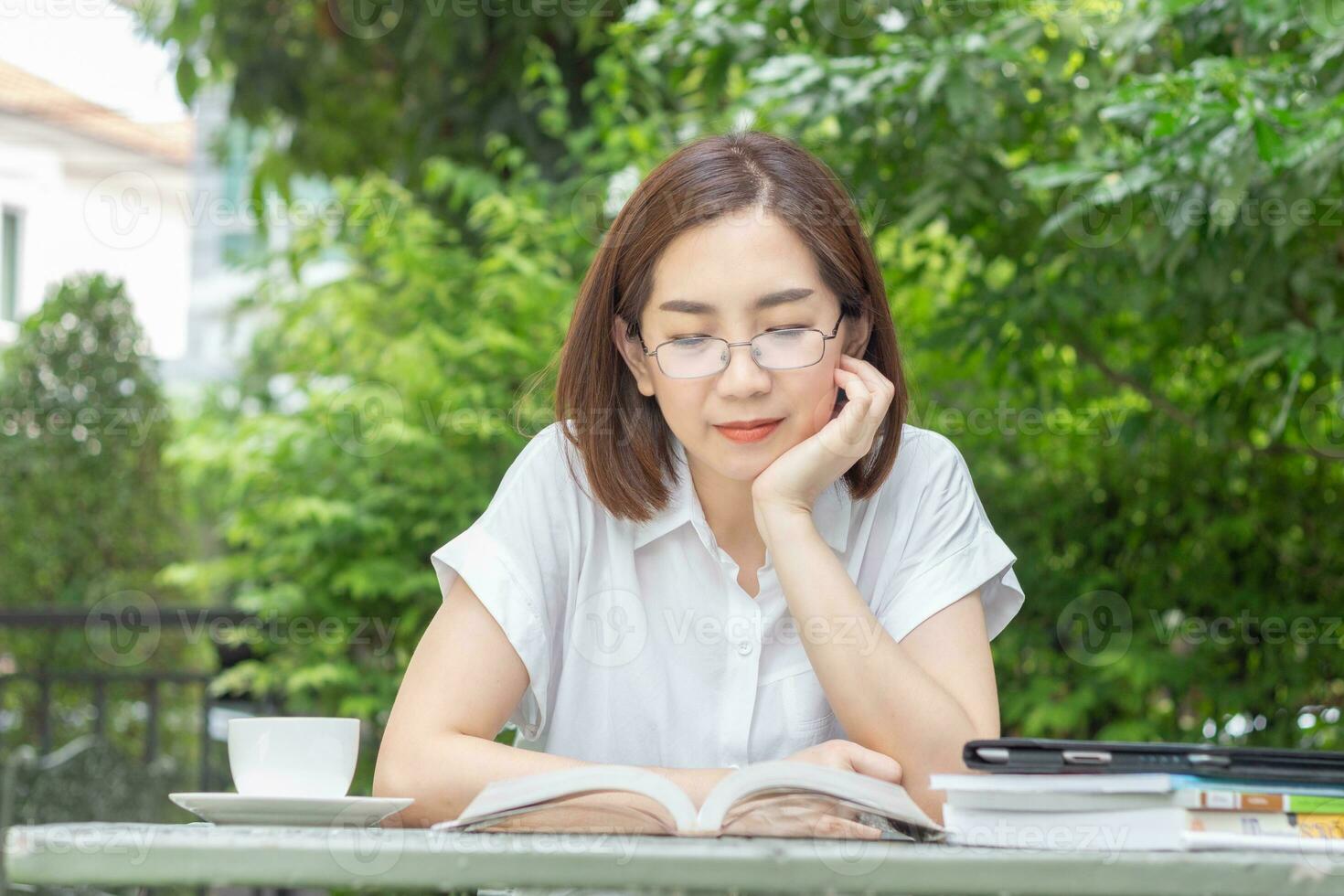 Asian middle aged woman in glasses reading a book in backyard photo